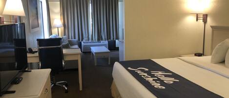 A hotel room with a bed, desk, chair, TV, and lamp.