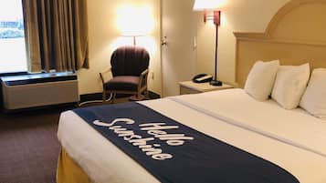 Une chambre d’hôtel avec un grand lit, une chaise, un bureau avec une lampe et une fenêtre avec des rideaux.