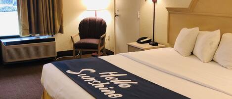 Ett hotellrum med en stor säng, en stol, ett skrivbord med en lampa och ett fönster med gardiner.