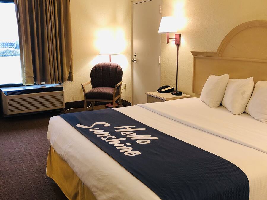 Una habitación de hotel con una cama grande, una silla, un escritorio con lámpara y una ventana con cortinas.