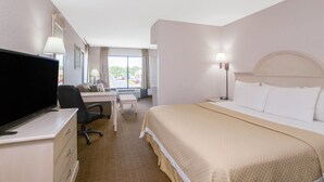 Ein Hotelzimmer mit einem Bett, einem Schreibtisch mit Stuhl, einem Fernseher und einem Fenster mit Vorhängen.