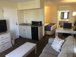 Une chambre d’hôtel compacte comprenant un coin cuisine, un lit avec une tête de lit, un canapé, une télévision et un bureau avec un ordinateur.