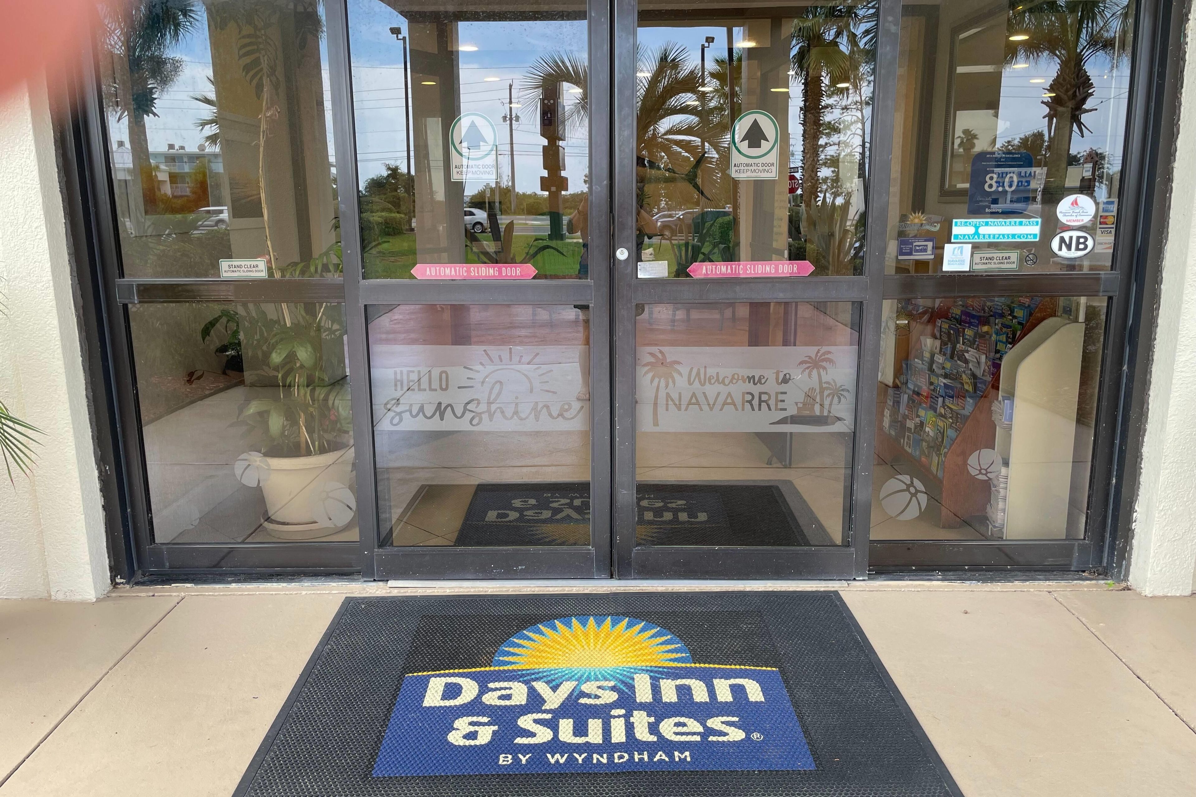A hotel entrance with automatic sliding doors, a welcome mat, and a sign for Days Inn & Suites by Wyndham.