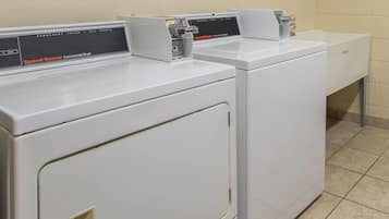 A row of white commercial dryers in a laundry room with a tiled floor.