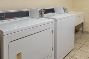 Une rangée de sèche-linge industriels blancs dans une buanderie dont le sol est carrelé.