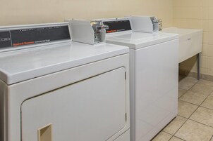 Une rangée de sèche-linge industriels blancs dans une buanderie dont le sol est carrelé.