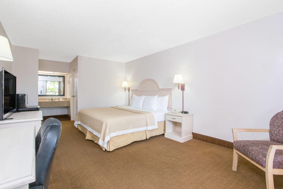 Ein Hotelzimmer mit Bett, Schreibtisch, Fernseher, Stuhl und Nachttisch mit Lampen.