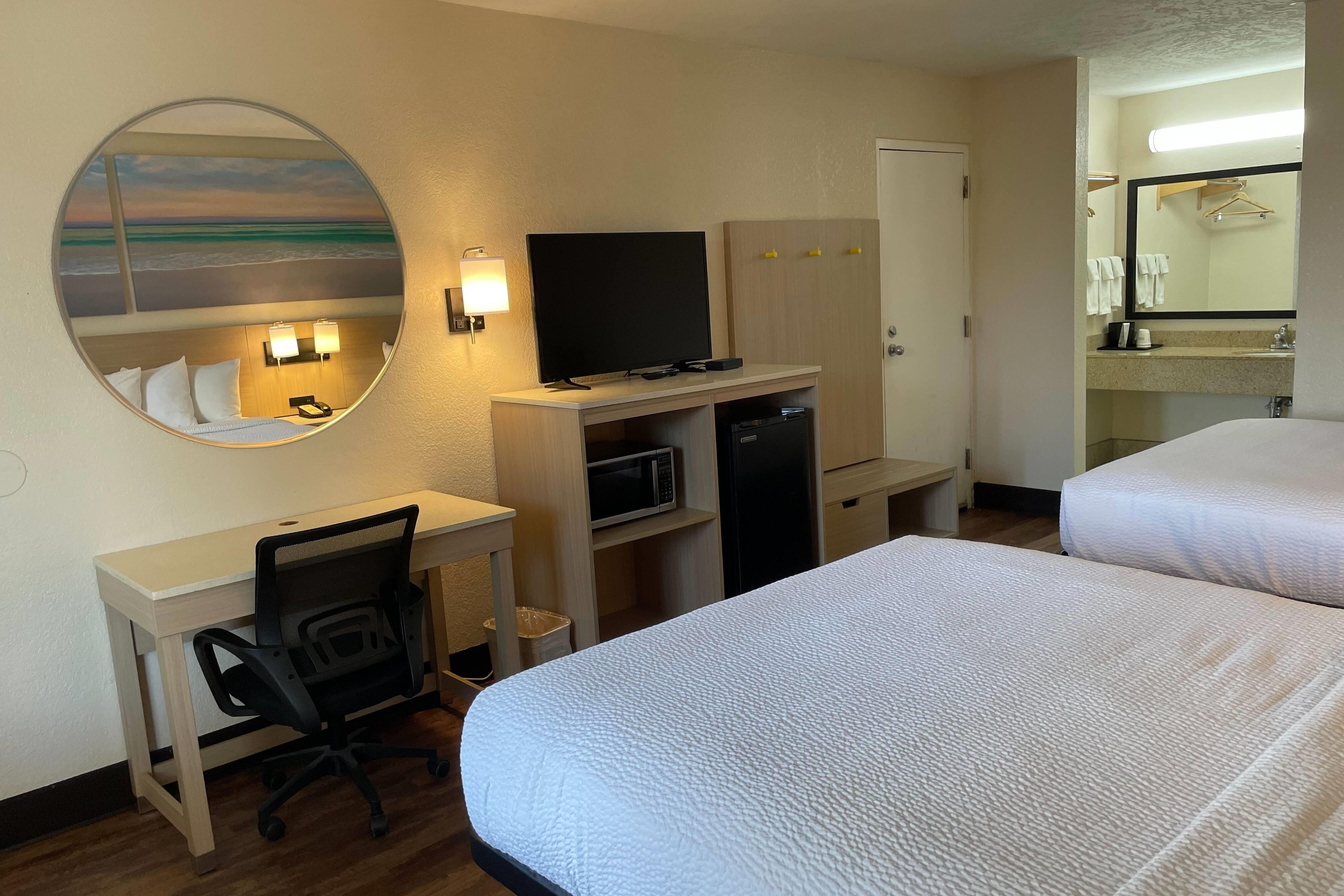 A hotel room with two beds, a desk with a chair, a television, a microwave, and a refrigerator.
