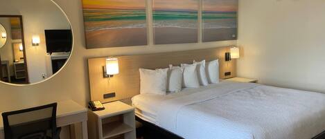 Een hotelkamer met een bed, bureau, stoel en kunstwerk aan de muur.