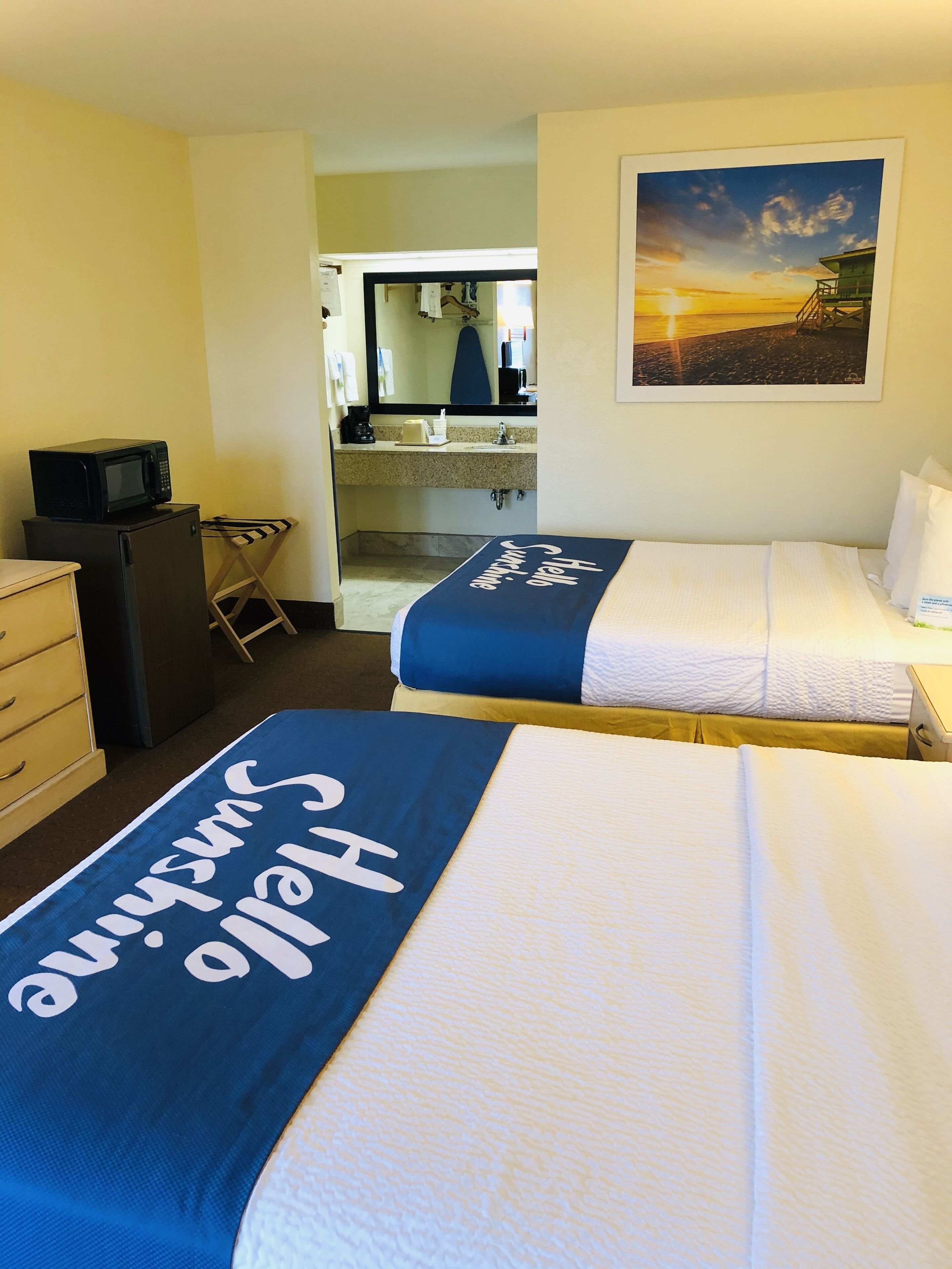 Quarto de hotel com duas camas, uma escrivaninha, micro-ondas e uma pequena cozinha.