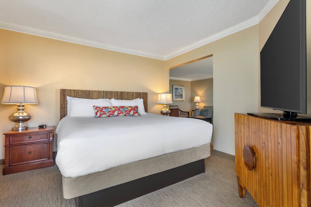 Een hotelkamer met een groot bed, houten nachtkastjes, een televisie en een spiegel.