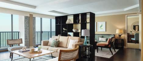 A spacious living room with a large window, a sofa, a coffee table, and a bookshelf.