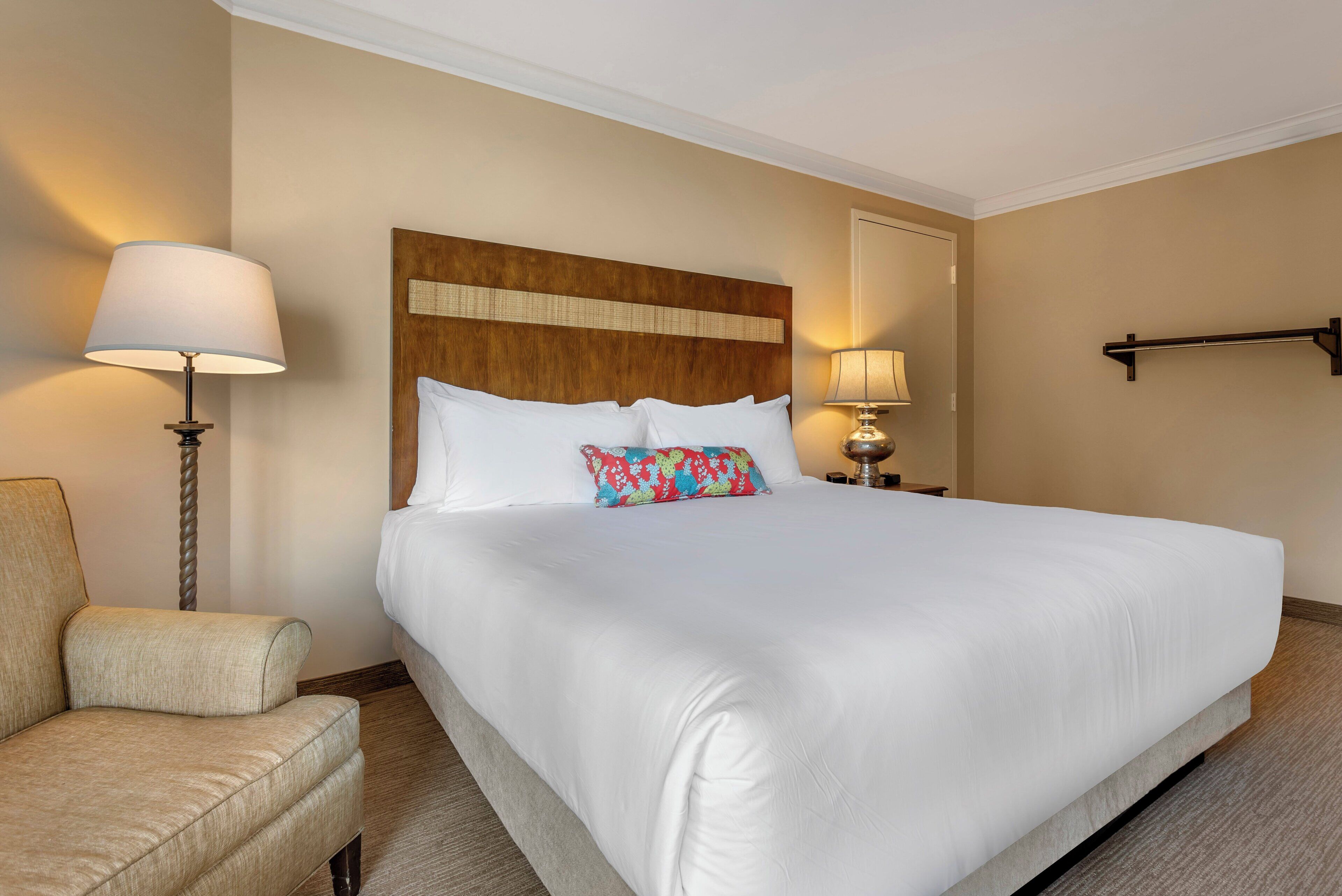 A hotel room with a large bed, a bedside table with a lamp, a chair, and a headboard with a decorative panel.