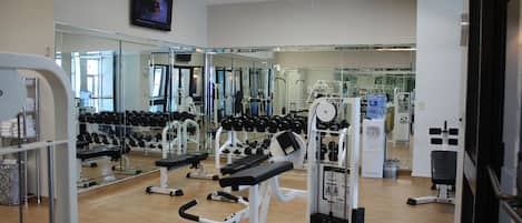 A gym with exercise equipment, mirrors, and a television.