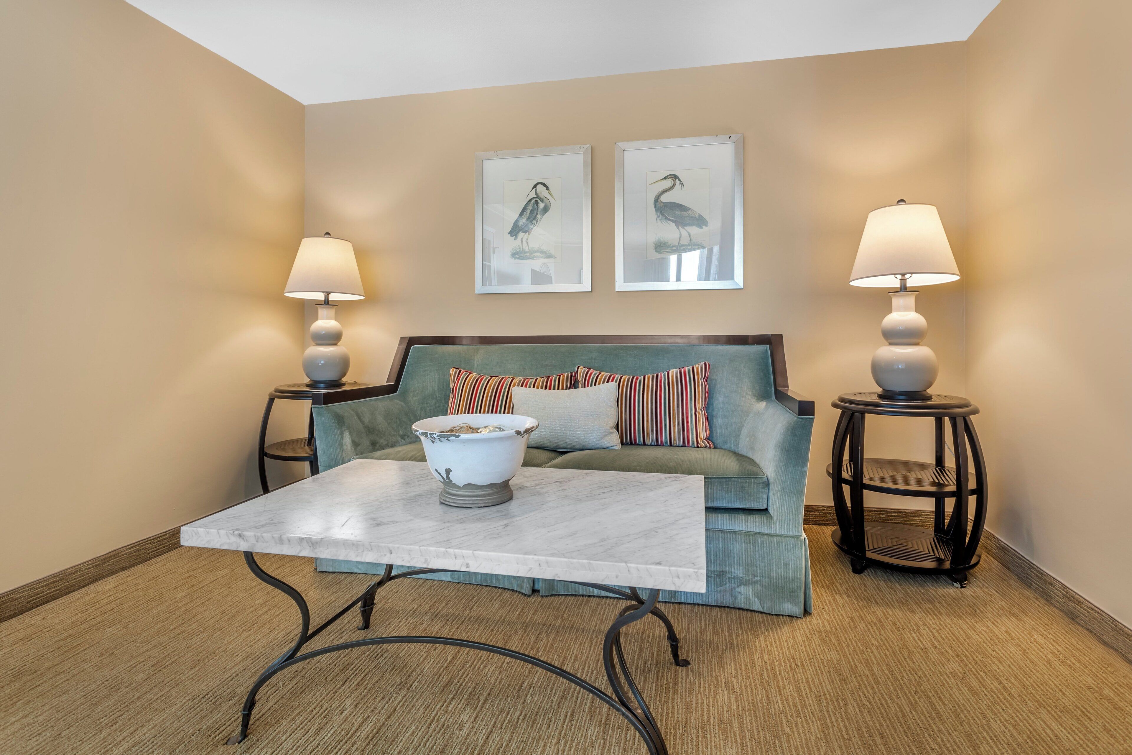A living room with a sofa, two lamps, a coffee table, and two wall-mounted bird paintings.