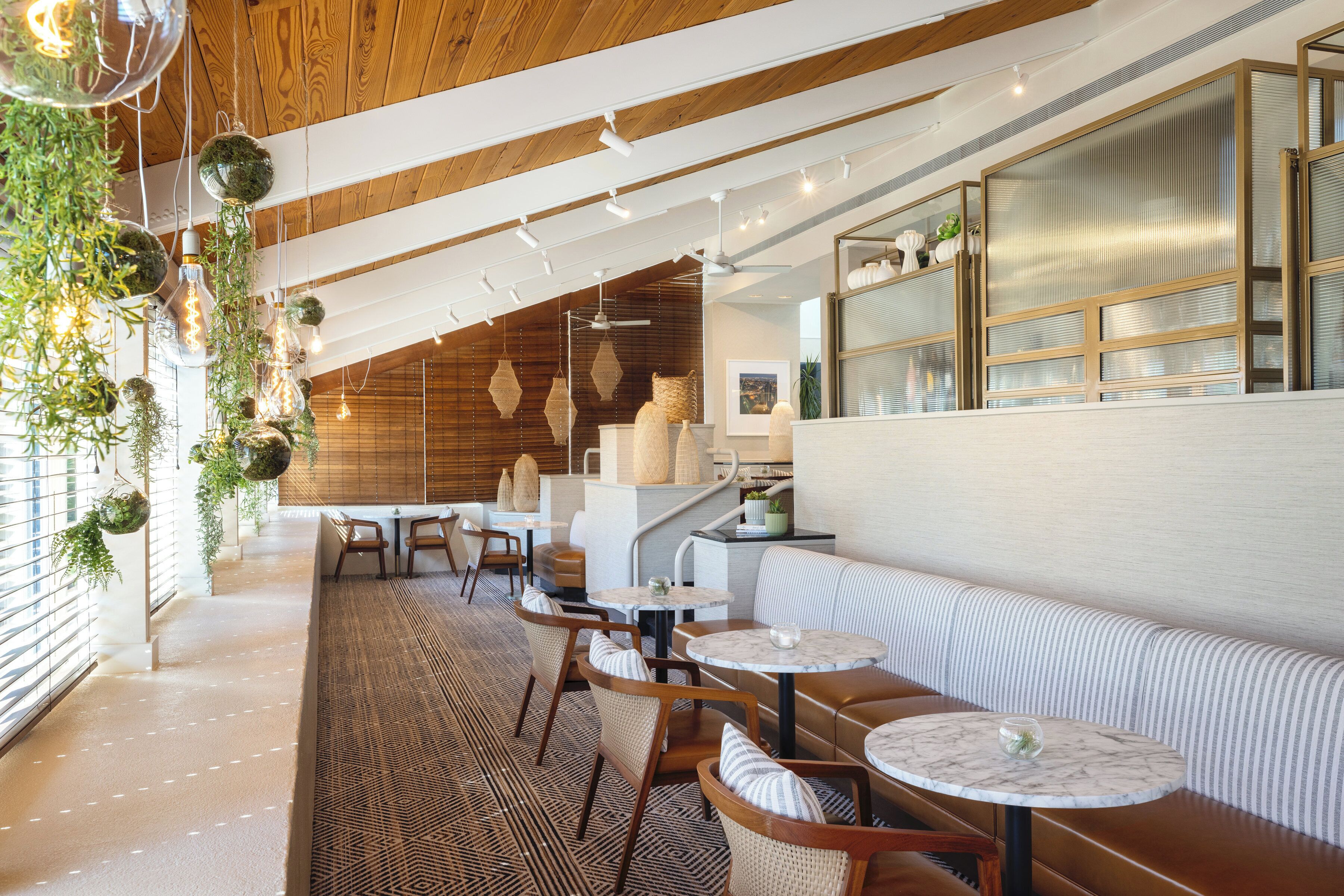 A modern interior with wooden ceiling beams, hanging plants, and a seating area with tables and chairs.