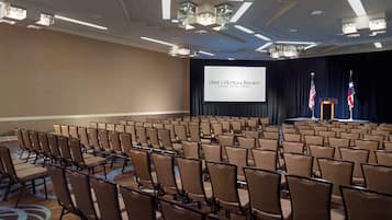 Une salle de conférence avec des rangées de chaises, une scène avec un pupitre et deux drapeaux.