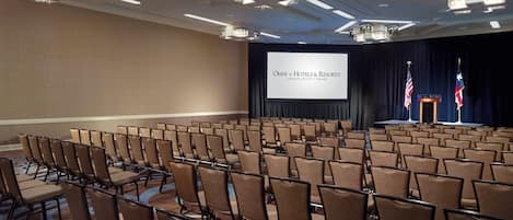 A conference room with rows of chairs, a stage with a podium, and two flags.