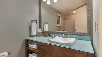 A bathroom with a glass countertop sink, wooden vanity, and a large mirror.