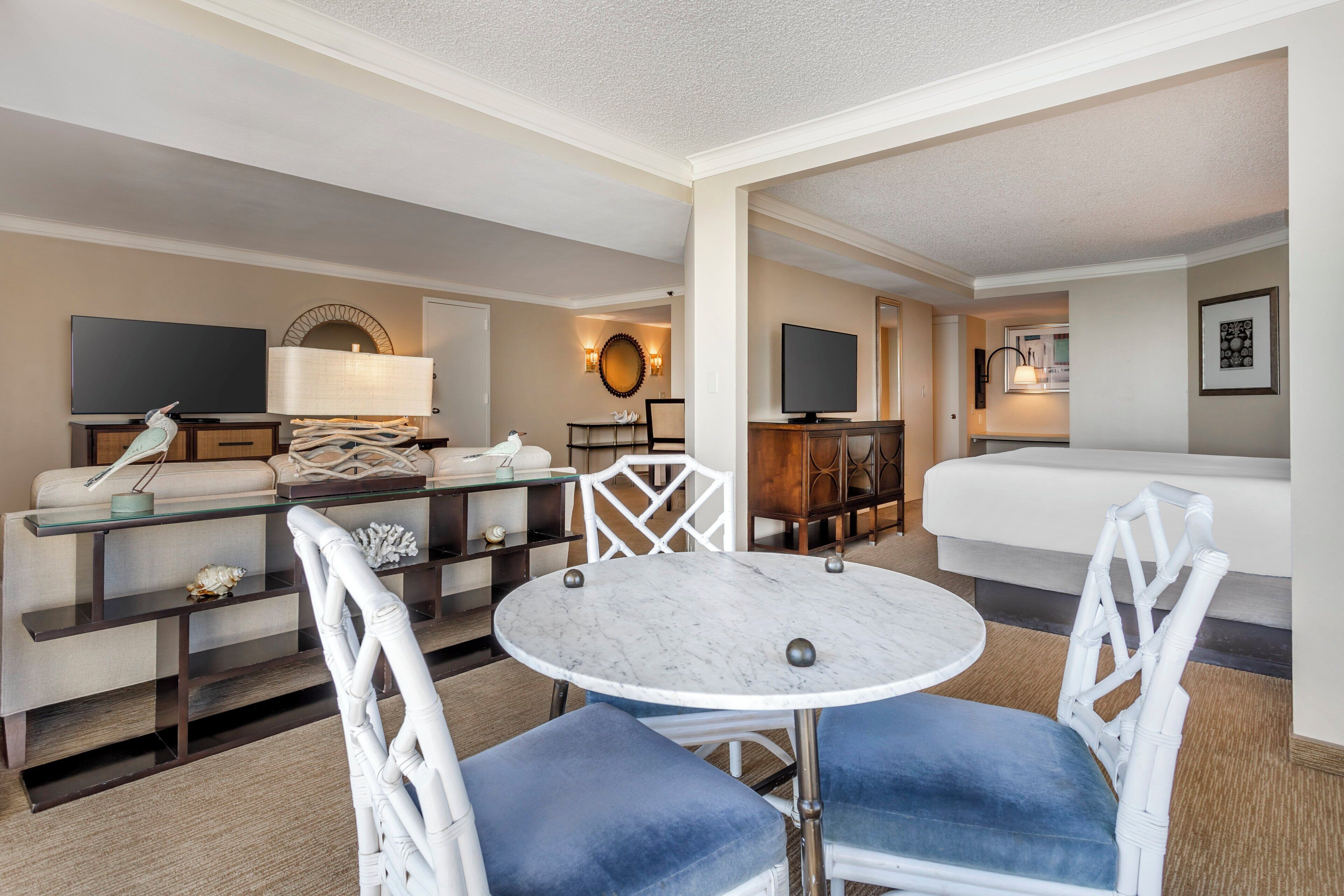 A hotel room with a bed, a TV, a dining table with chairs, a sofa, and a lamp.