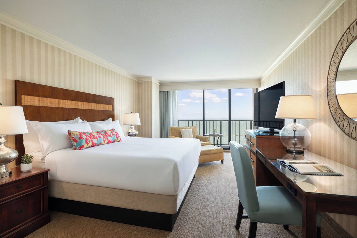 Een hotelkamer met een groot bed, een bureau, een stoel, een televisie en een balkon met uitzicht.