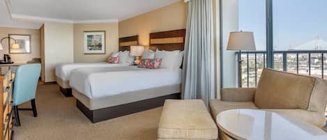 A hotel room with two beds, a desk, a chair, a sofa, and a balcony with a view of a bridge.