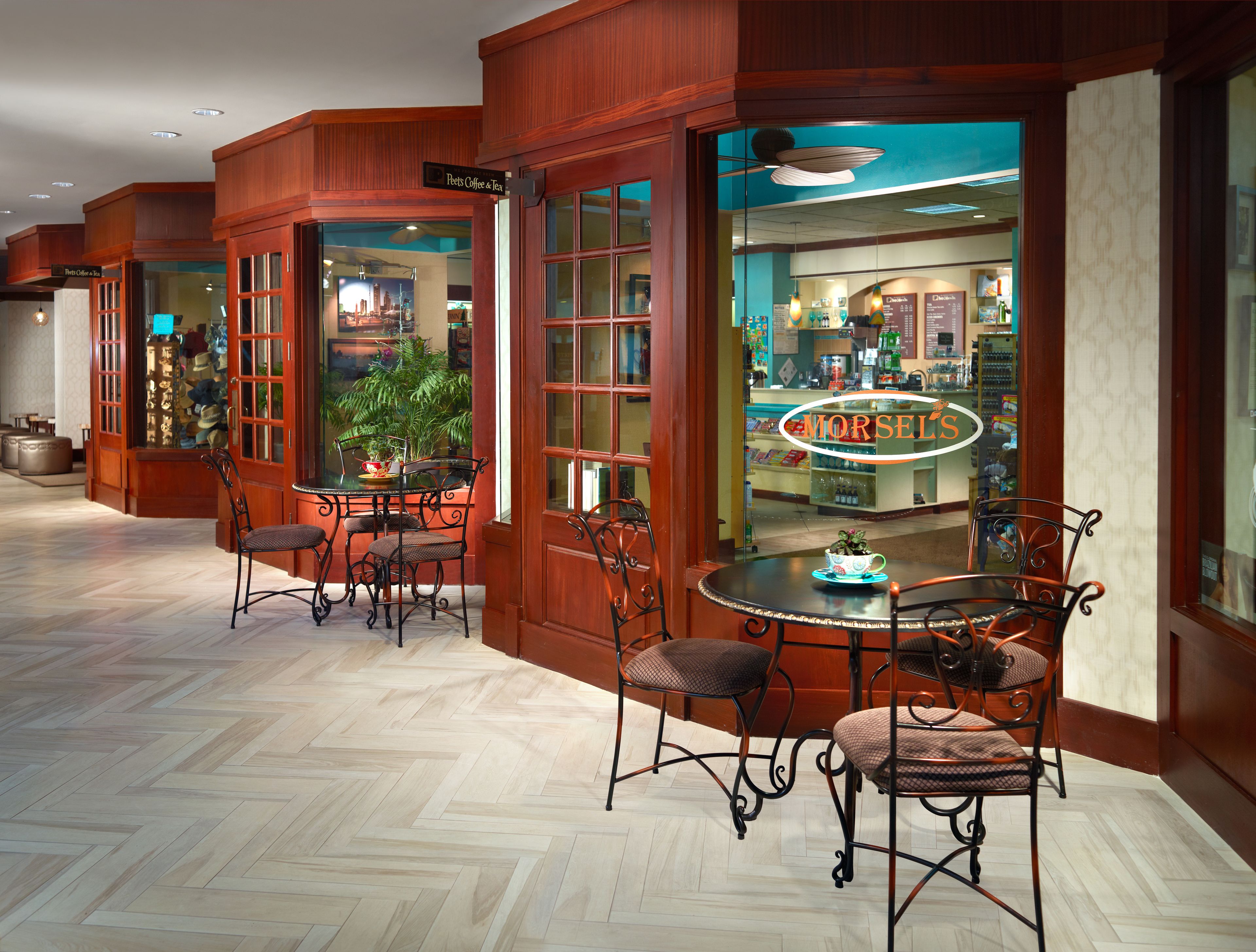 A hotel lobby with a coffee shop, wooden flooring, and a seating area with metal chairs.