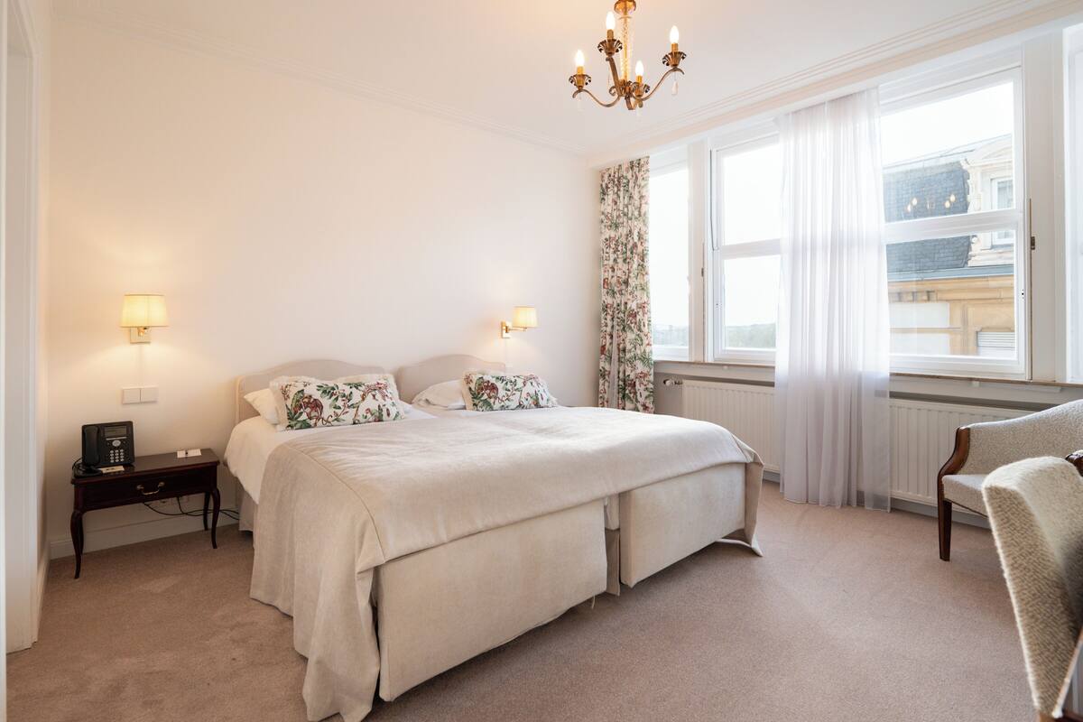 Ein Schlafzimmer mit einem großen Bett, Nachttischlampen, einem Telefon und Blick auf die Stadt durch das Fenster.