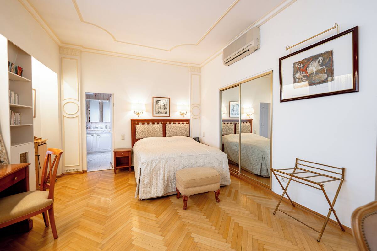 Ein Schlafzimmer mit Bett, Stuhl, Kleiderschrank, Spiegel und Wäscheständer.