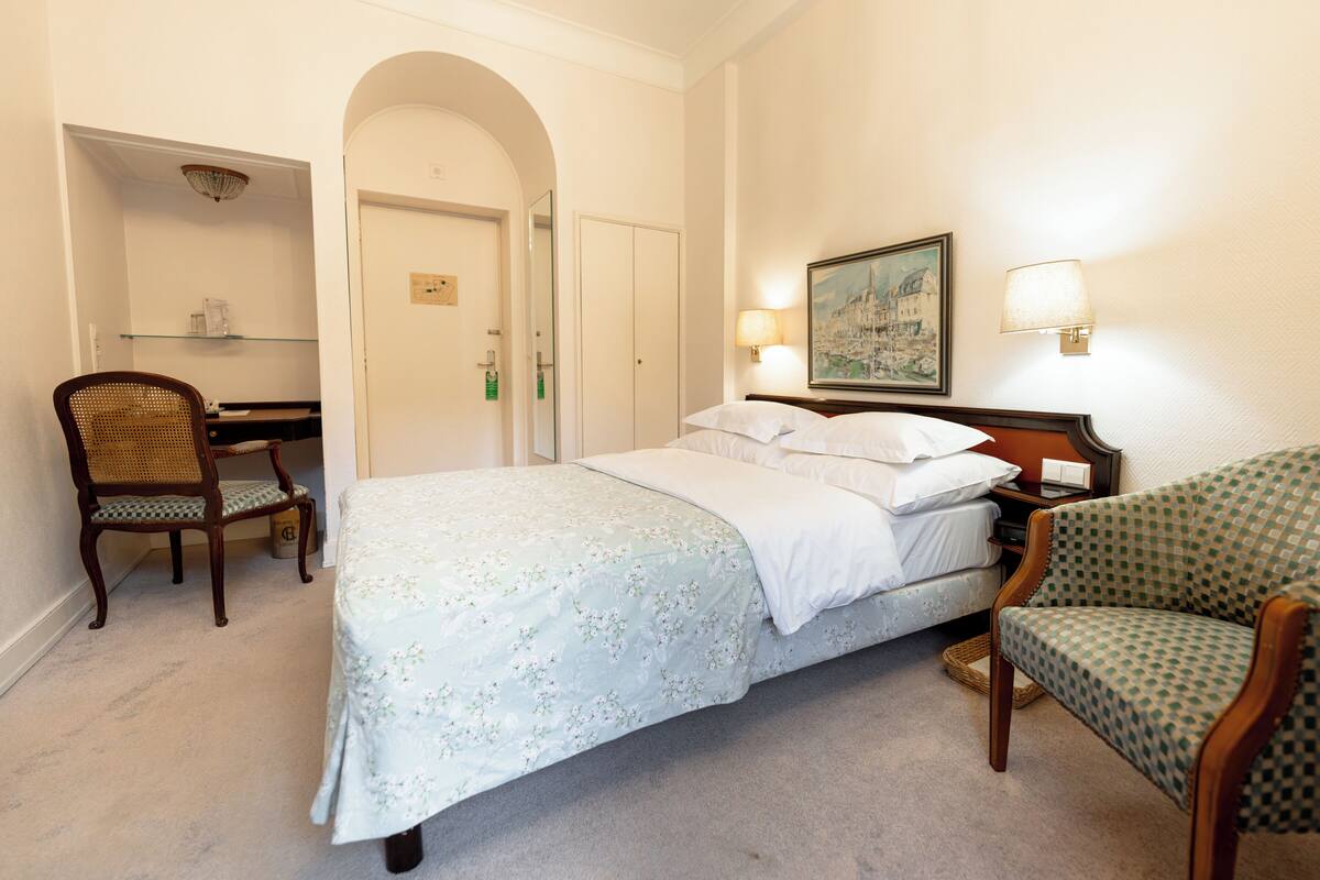 Ein Hotelzimmer mit Bett, Schreibtisch, Stuhl und einem Gemälde an der Wand.