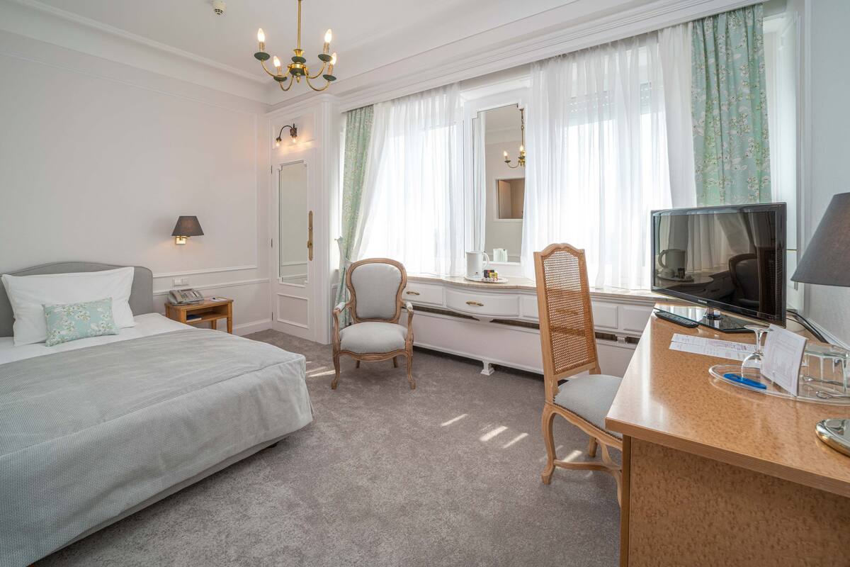 Ein Hotelzimmer mit einem Bett, einem Schreibtisch mit Computer, einem Sessel, einem Schminktisch und einem großen Spiegel.