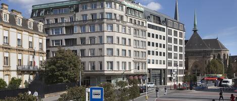 A multi-story hotel with a prominent corner location, a large entrance, and a visible church spire in the background.