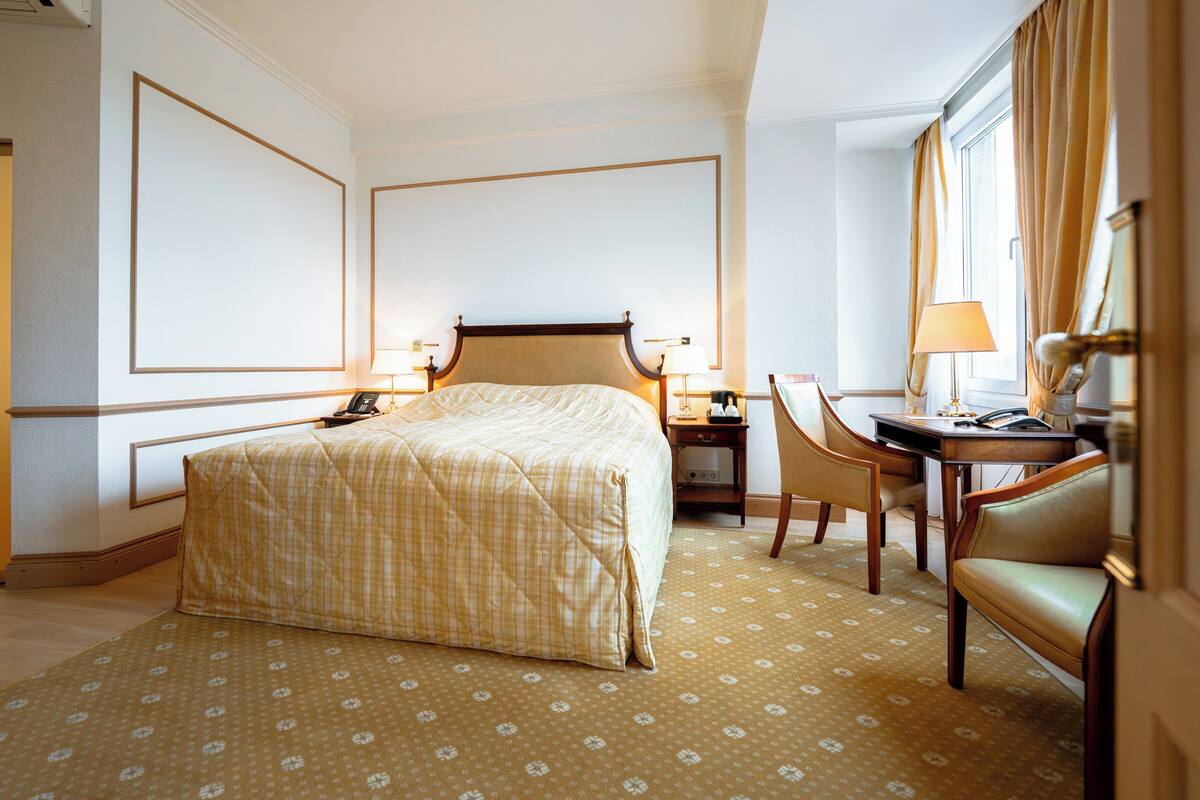 Ein Hotelzimmer mit Bett, Schreibtisch mit Stuhl, Telefon und einem Fenster mit Vorhängen.