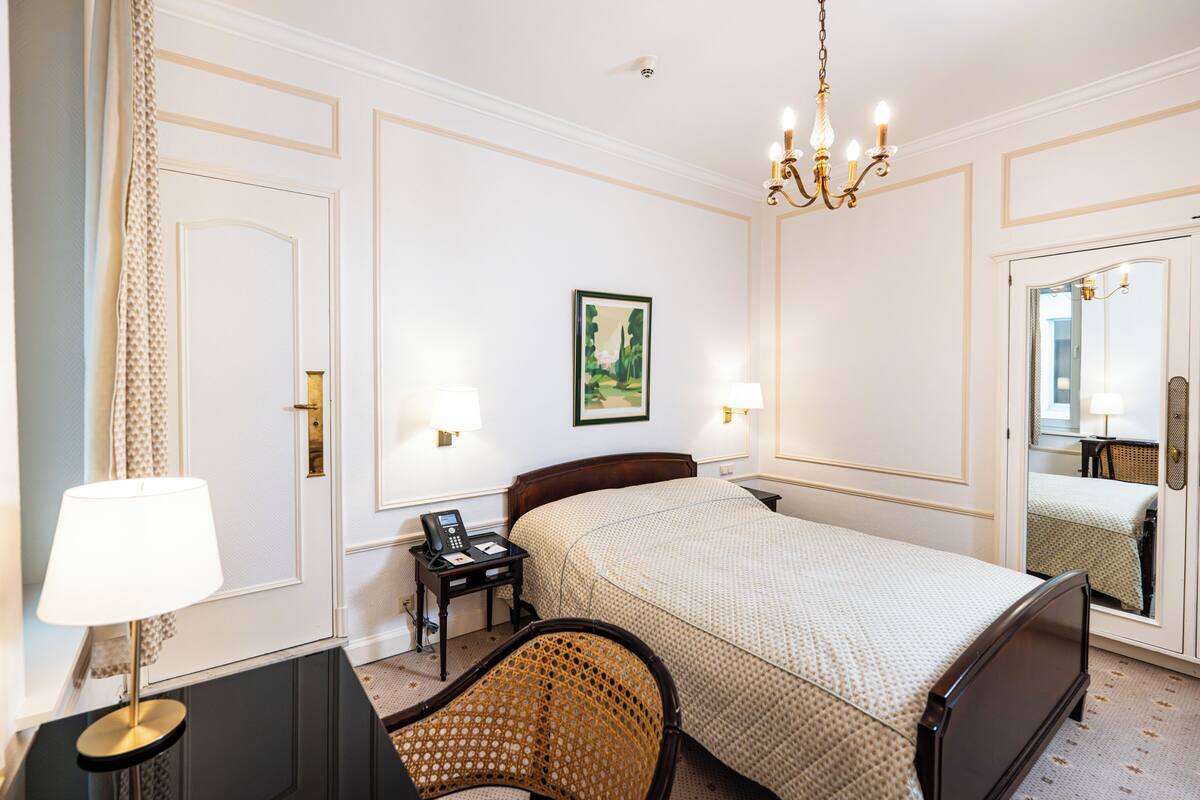 Ein Hotelzimmer mit Bett, Nachttisch, Lampe, Stuhl, Schreibtisch und einem Bild an der Wand.