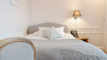Een net opgemaakt bed met kussens, een bedlampje en een telefoon op een houten nachtkastje.