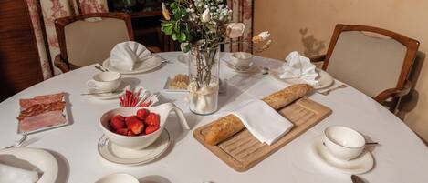 A round table set with breakfast items, including bread, strawberries, and a vase with flowers.