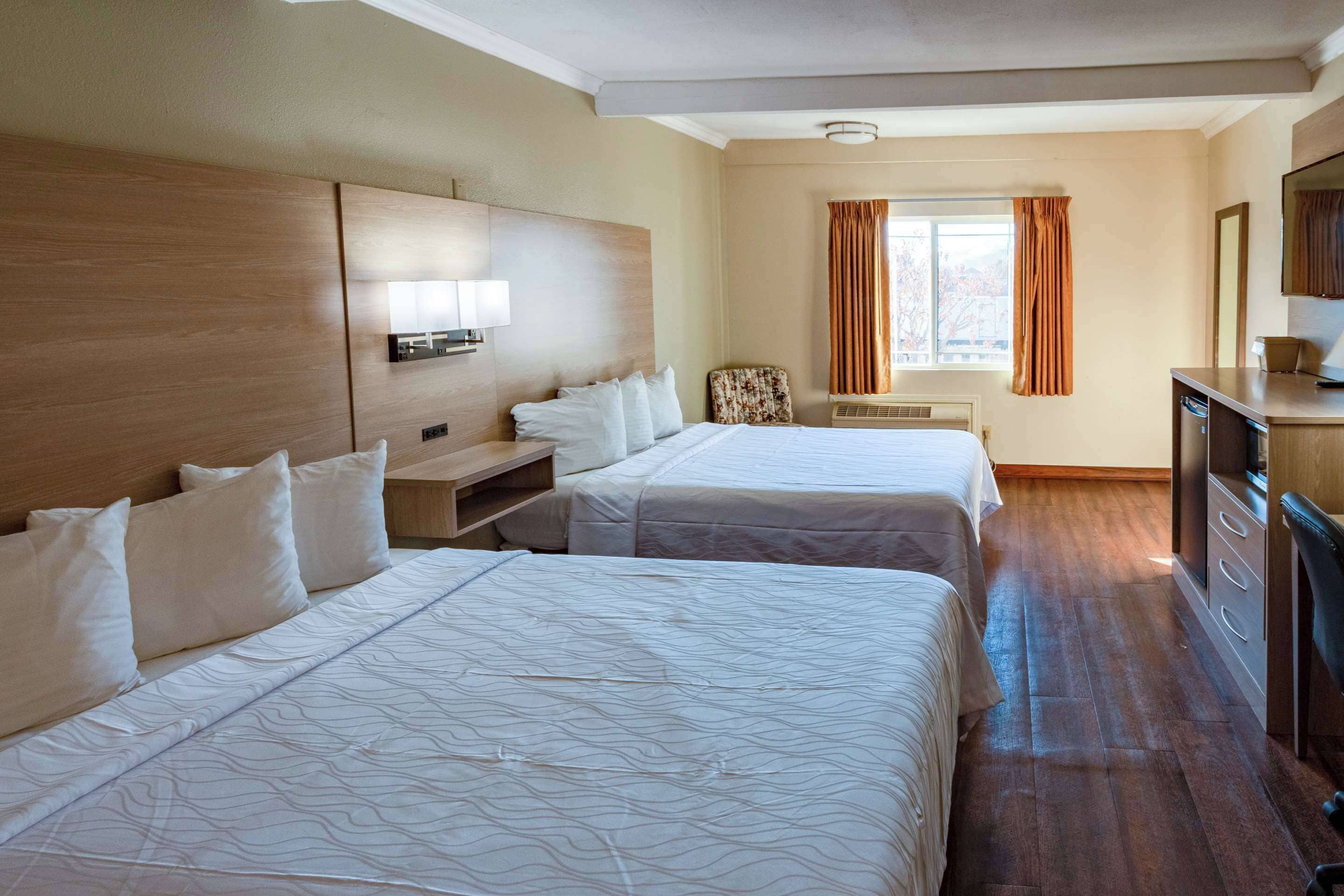 A hotel room with two beds, a desk, a chair, a dresser, and a window with curtains.