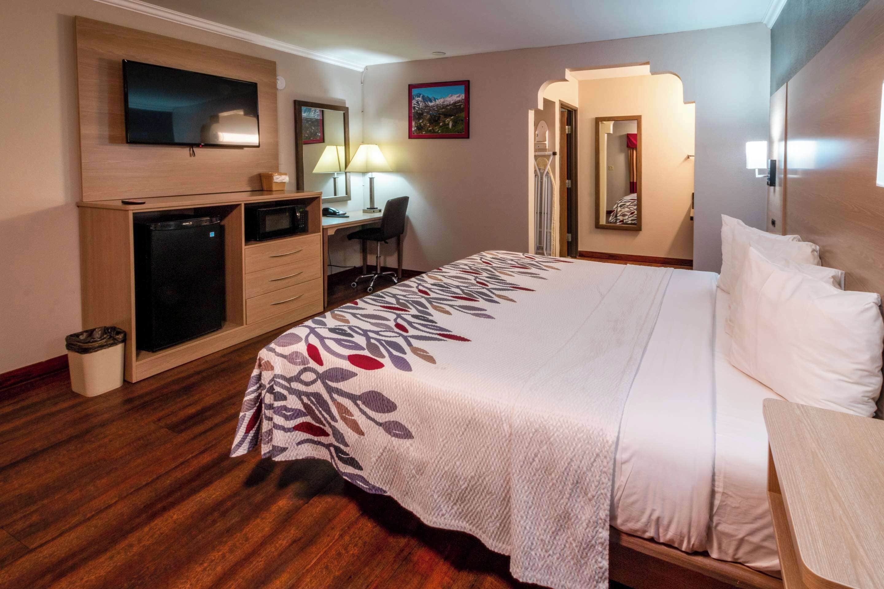 Une chambre d’hôtel avec un lit, un bureau, une télévision et un miroir.