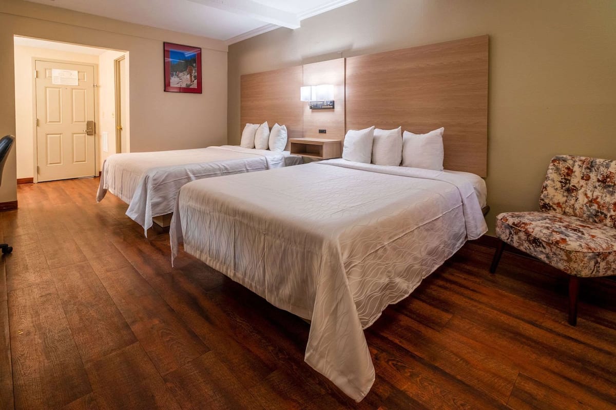 Una habitación de hotel con dos camas, cabecera de madera, una silla y una puerta.