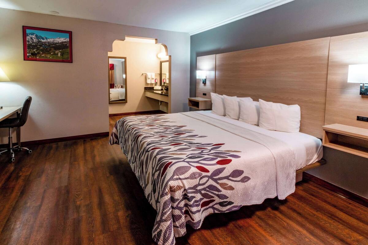 Habitación de hotel con una cama grande, un escritorio y un baño visible a través de una puerta abierta.
