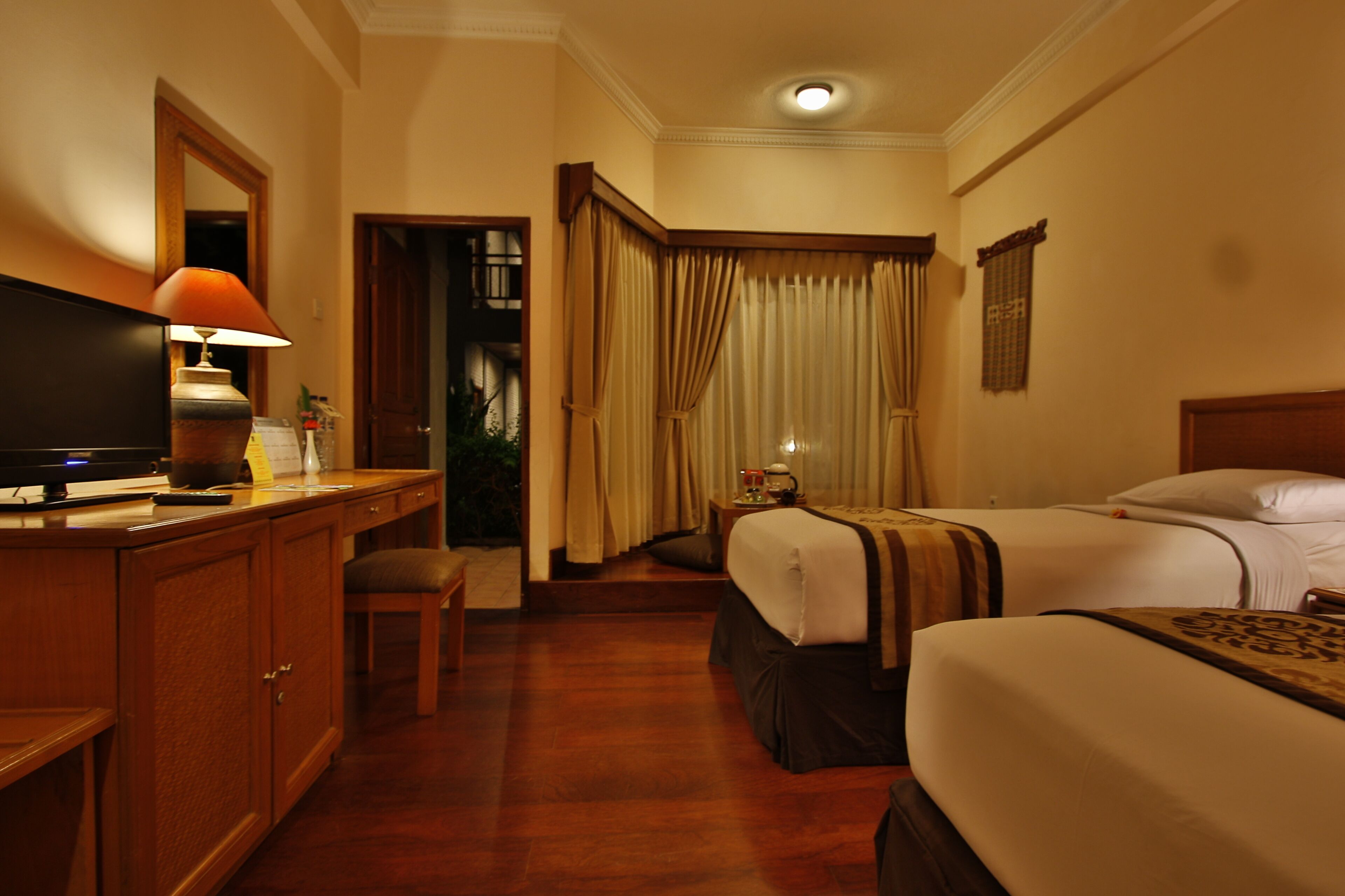 Habitación de hotel con un escritorio de madera, un televisor, dos camas, una mesita de noche y un baño visible a través de una puerta.