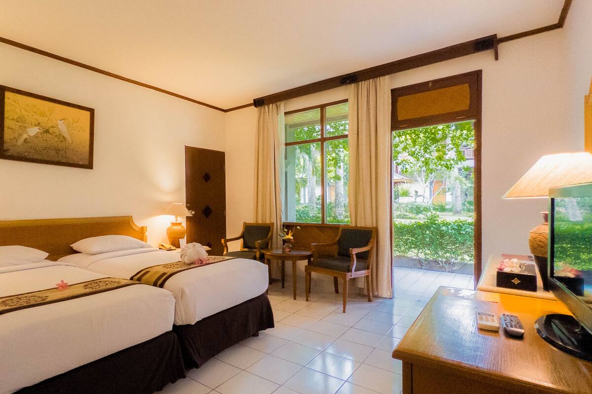 Ein Hotelzimmer mit zwei Betten, einem Schreibtisch mit Lampe, einem Stuhl und einem Fenster mit Vorhängen.