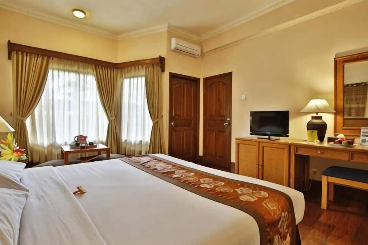 Une chambre dâhĂŽtel avec un grand lit, un bureau, une tĂ©lĂ©vision et une fenĂȘtre avec des rideaux.
