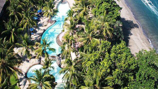 Luchtbeeld van een resort met een zwembad, palmbomen en een strand.