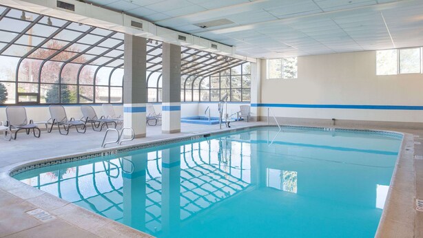 An indoor swimming pool with clear blue water, sunlit by large windows, and surrounded by lounge chairs. - Ramada by Wyndham Downtown Spokane (Spokane)