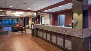 A reception area with a wooden floor, a reception desk, and a seating area with chairs. - Ramada by Wyndham Downtown Spokane (Spokane)