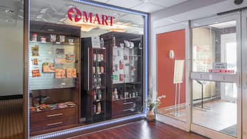 Una tienda con un llamativo letrero 'OMART', estantes llenos de aperitivos y bebidas, y una puerta corredera automática.