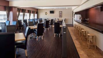 A modern hotel lobby with a long reception desk, multiple seating areas with tables and chairs, and a bar area with stools.