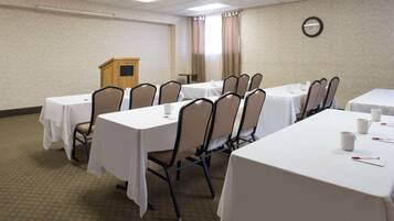 A conference room with multiple tables and chairs, a podium, and a clock on the wall.