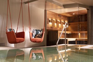 Un moderno espacio de spa con un jacuzzi de paredes de vidrio, paneles de madera y dos sillones de mimbre.